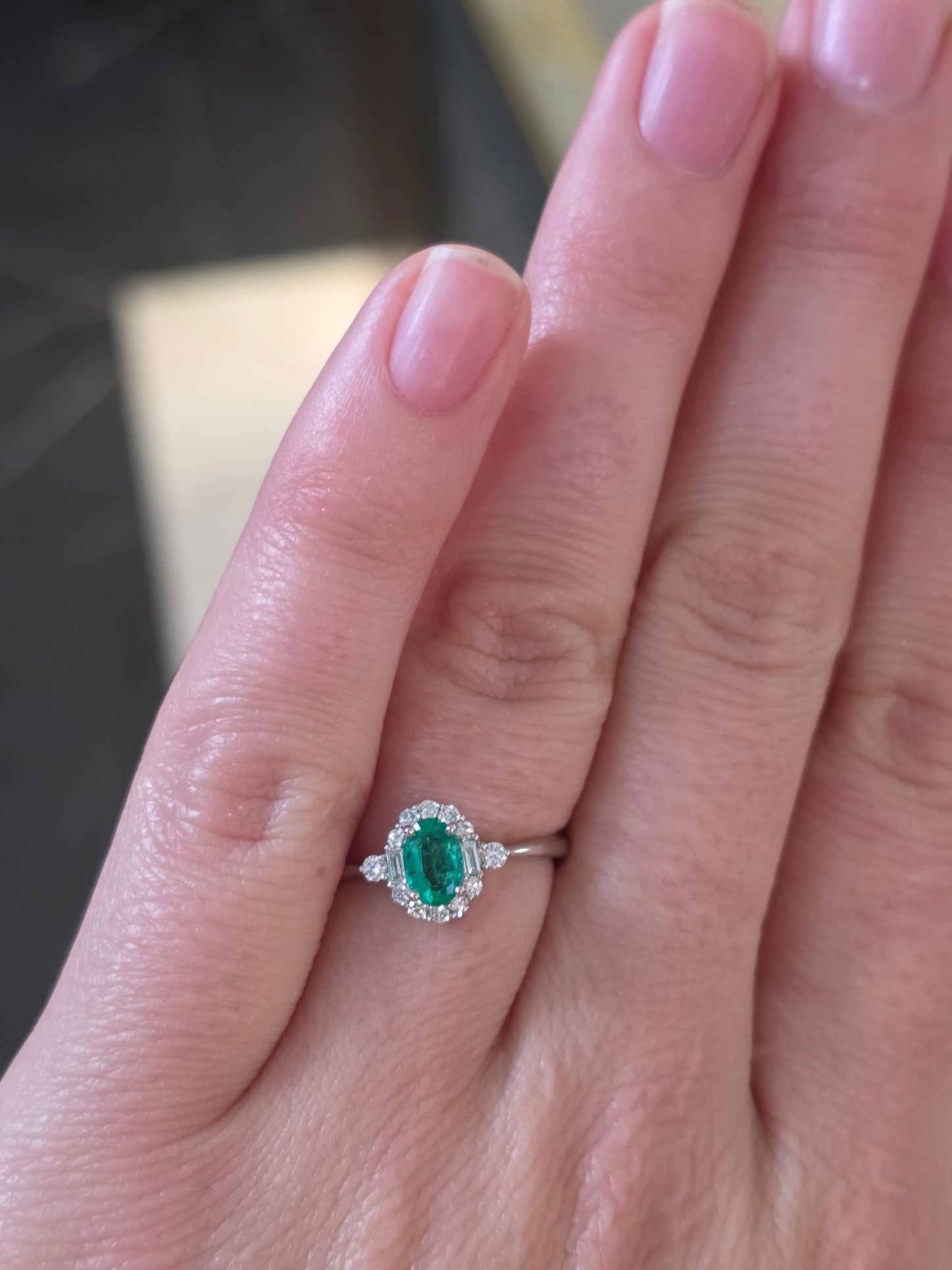 Close-up of a hand wearing an emerald ring with a blurred background